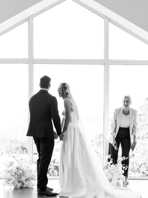 A black-and-white photograph of Jasmine and Joshua standing together inside a light-filled wedding chapel.