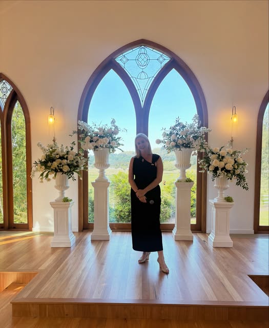 Bec standing between floral arrangements inside the chapel at The Valley Estate.