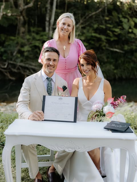 Bec with Rory and Tory seated at their outdoor wedding signing table.