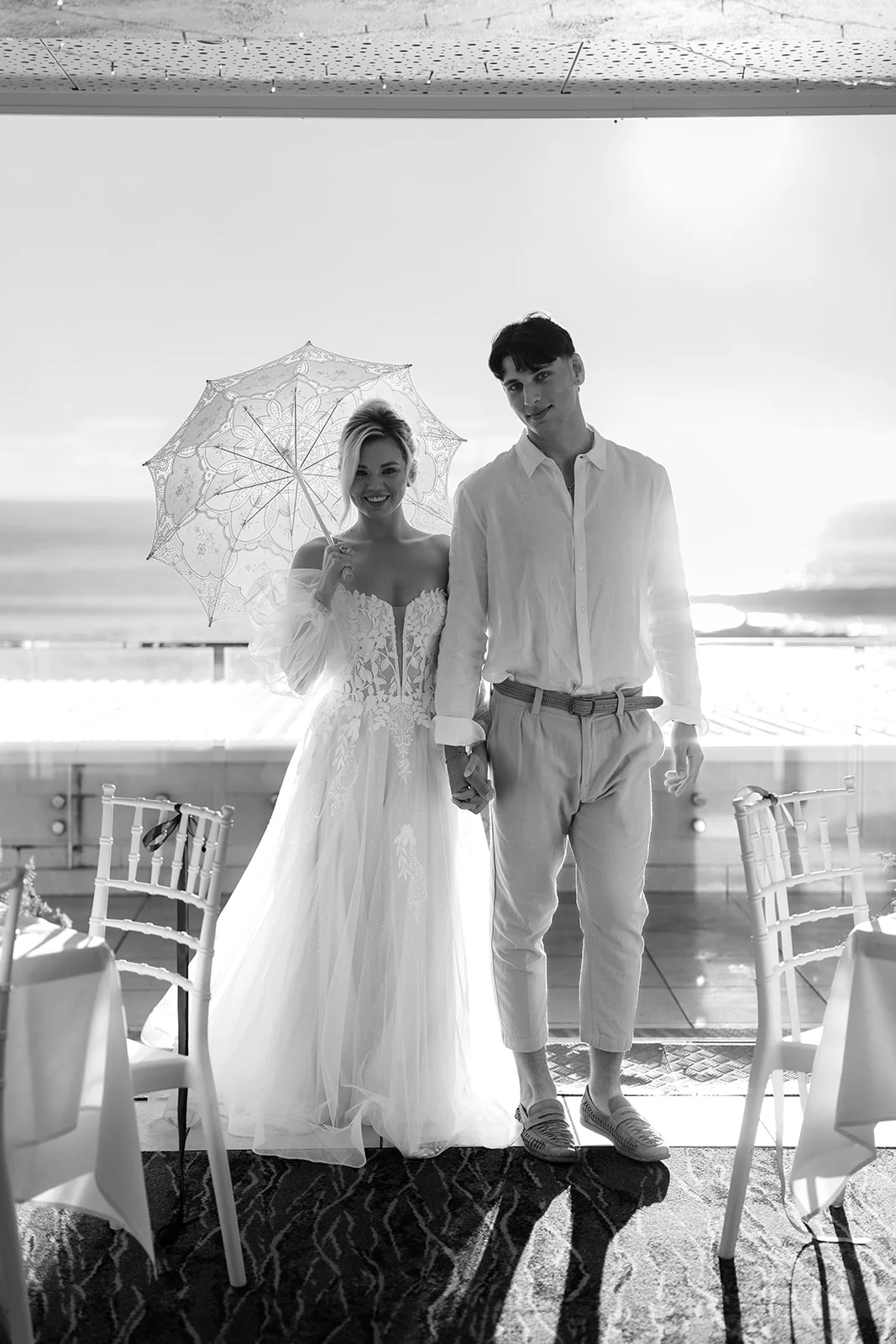A couple beneath a parasol at their coastal wedding